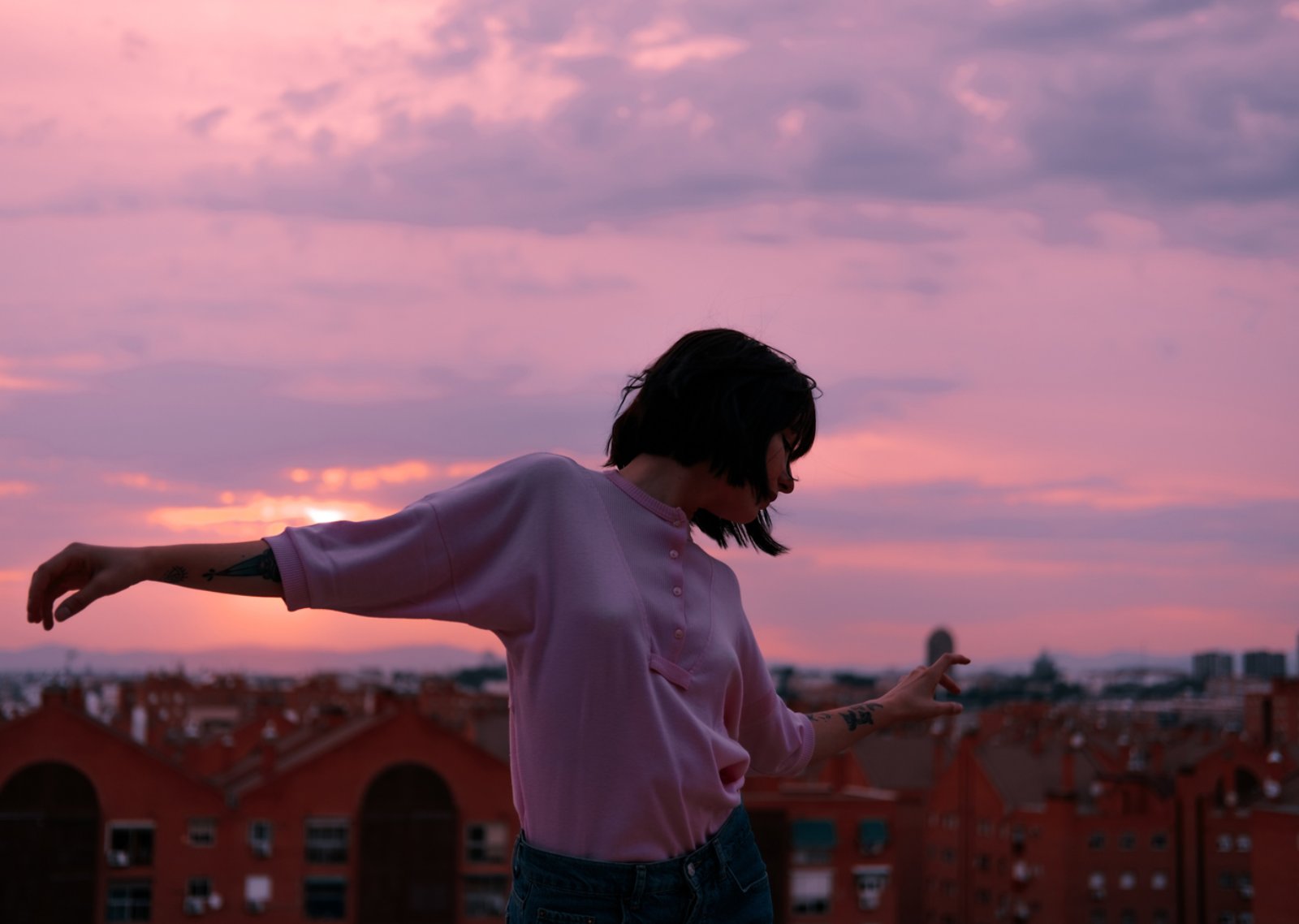 Eine Frau fühlt sich frei in der lila Morgendämmerung, genießt die Sicht auf die Stadt und tanzt.