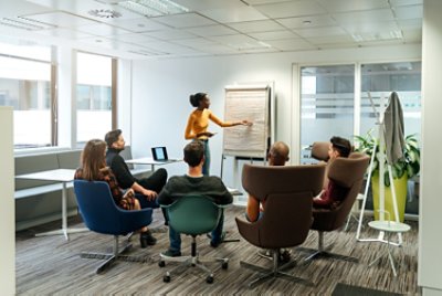 Group Of Business Partners Listening To Presentation With Flip Chart At Office