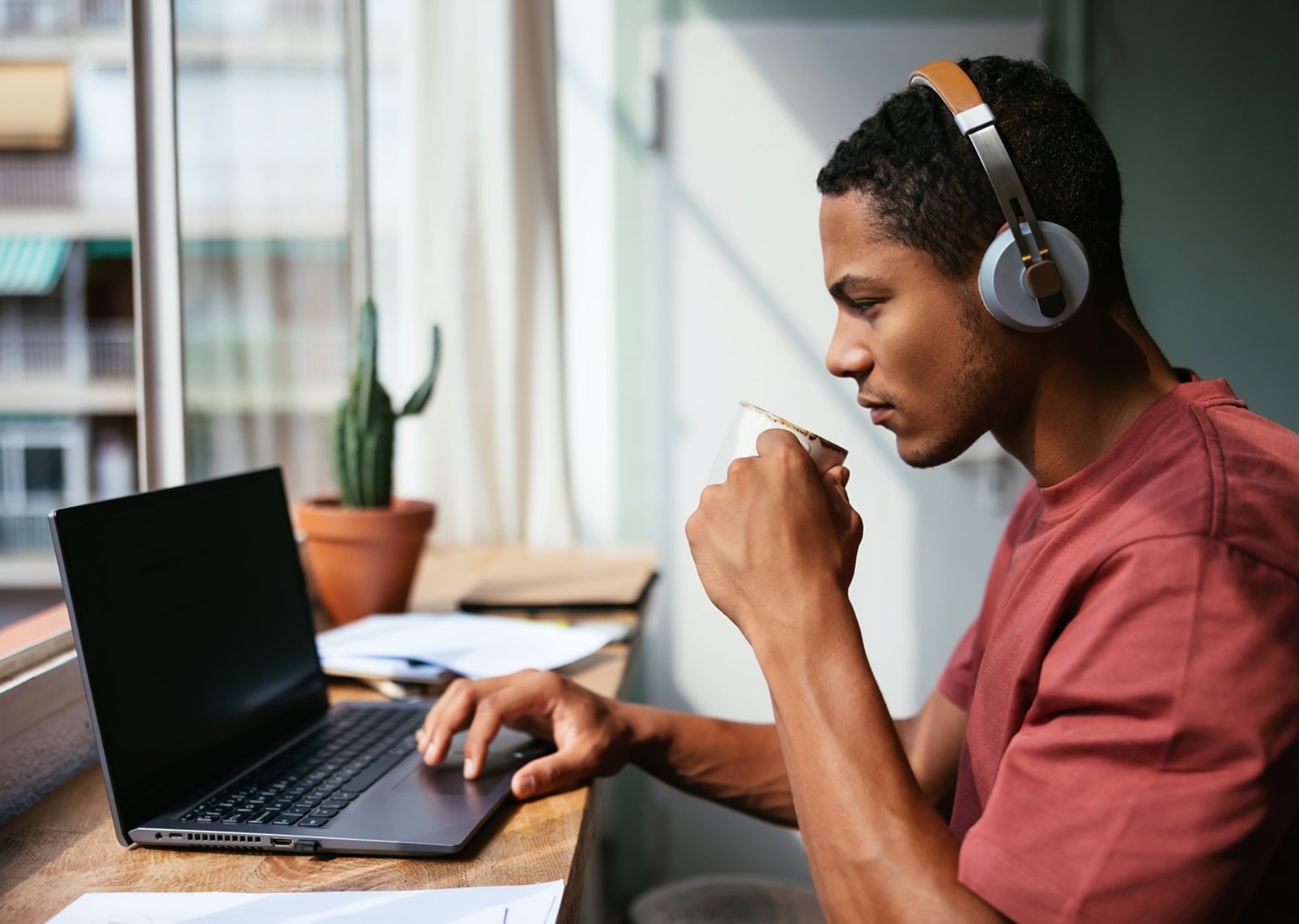 Sipping hot drink and listening to music while browsing data on laptop during work on remote project at home.