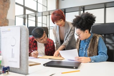 Teamwork Between Three Colleagues At Office Desk.