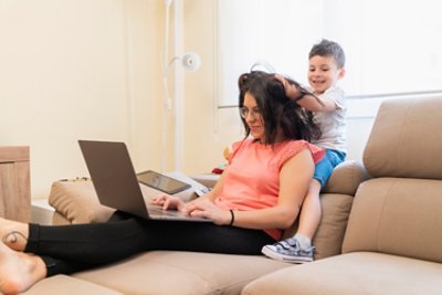 A mother using her laptop while her son is holding her hair