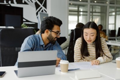 Partner office analyse business associate paper. Multiethnic fellow workers in good mood, sitting close to each other at table with electronics, examining reports closely and pondering over it together in headquarters.