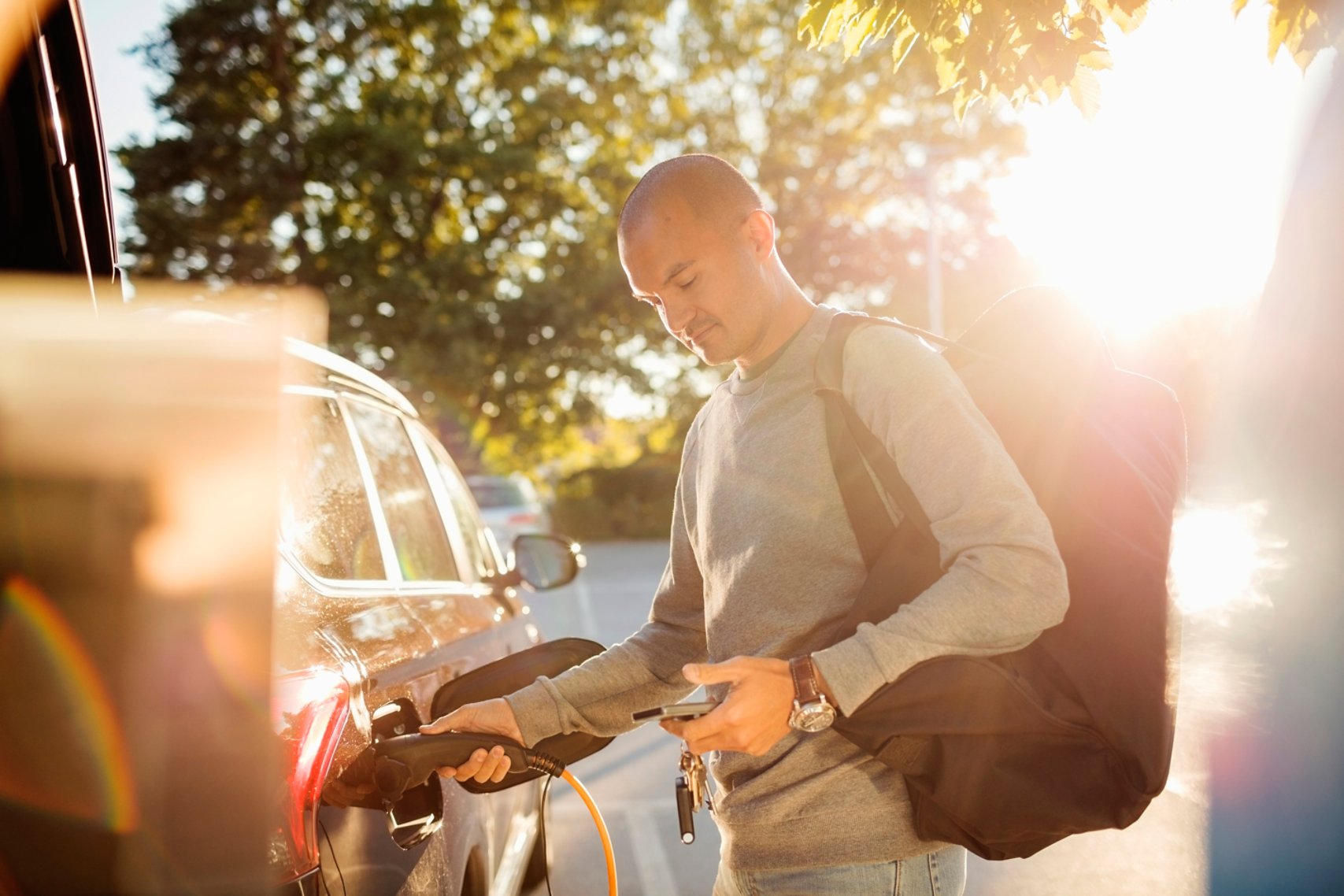 A man fueling his car while holding a phone