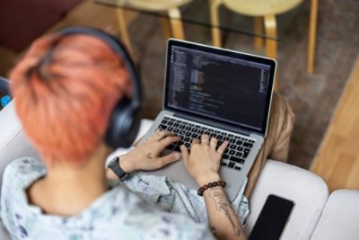 Over the shoulder view of a man coding on his laptop while sitting at the office. Software engineer with headphones working on laptop while sitting at office.