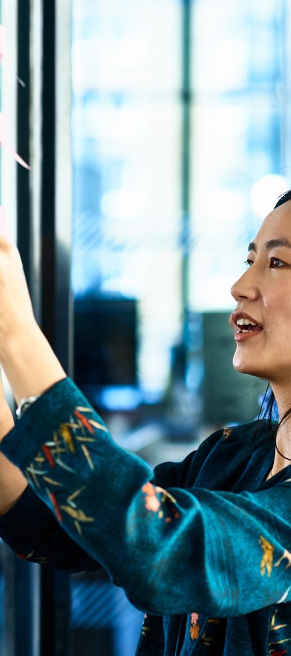A woman is collaborating with a man by writing notes on a glass wall in an office