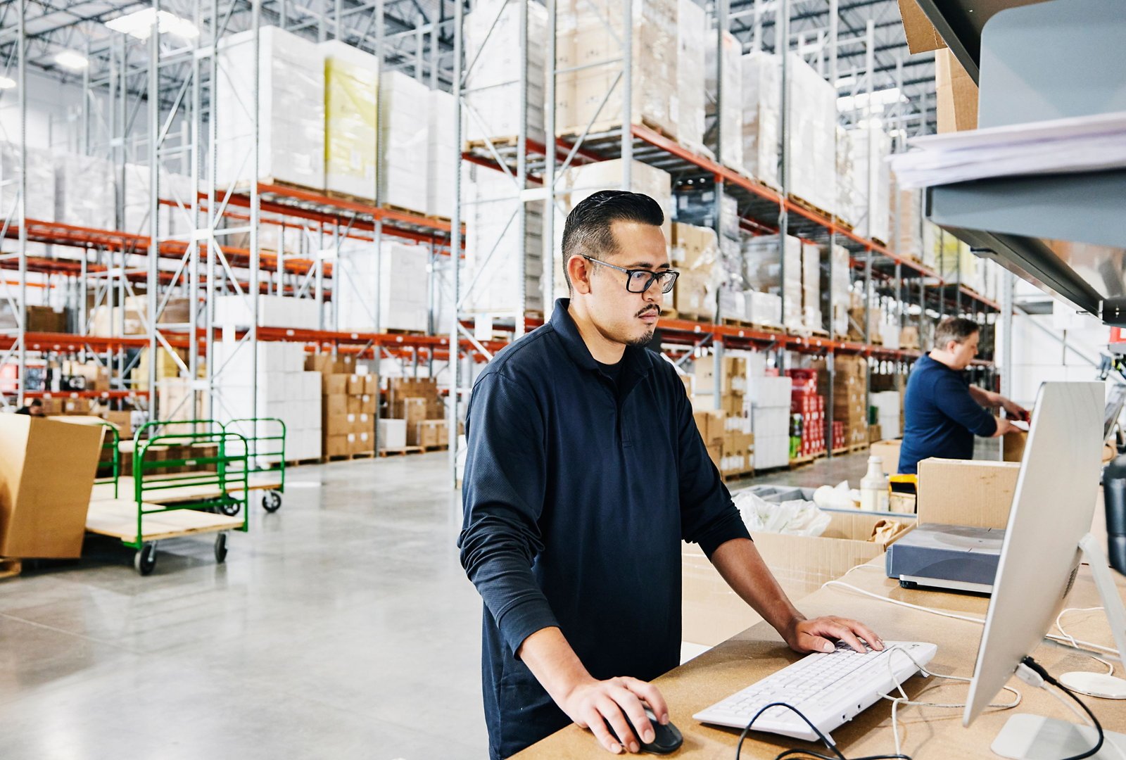Male warehouse worker checking orders at computer workstation in warehouse