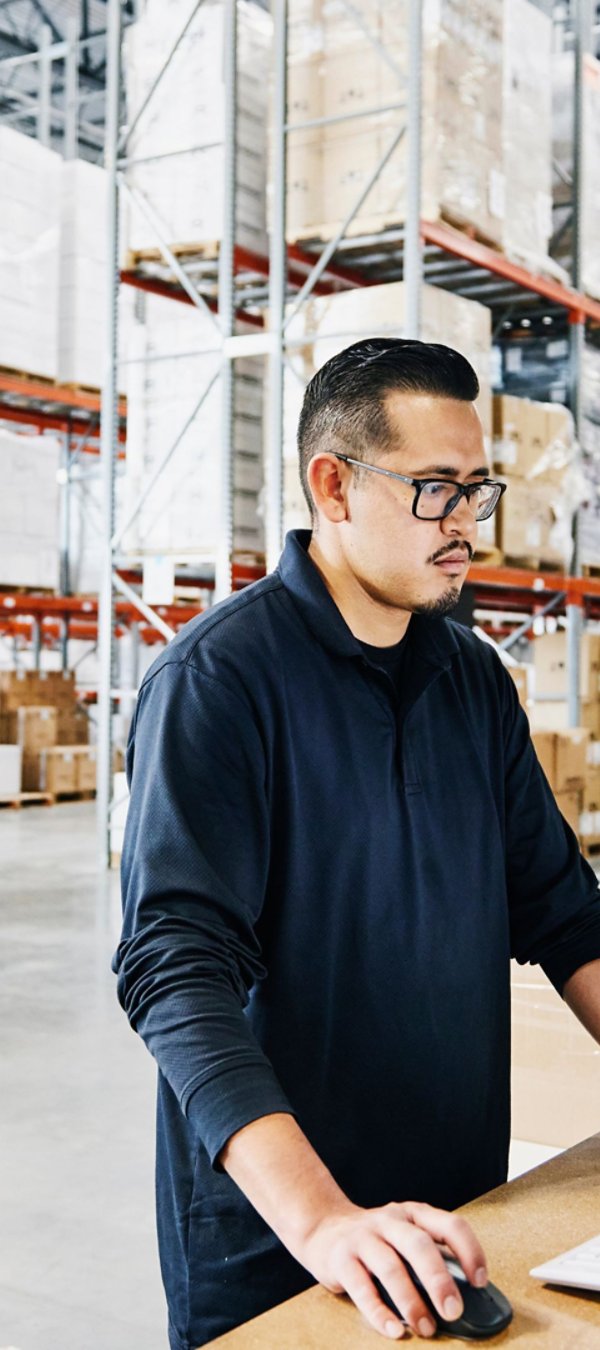 Male warehouse worker checking orders at computer workstation in warehouse