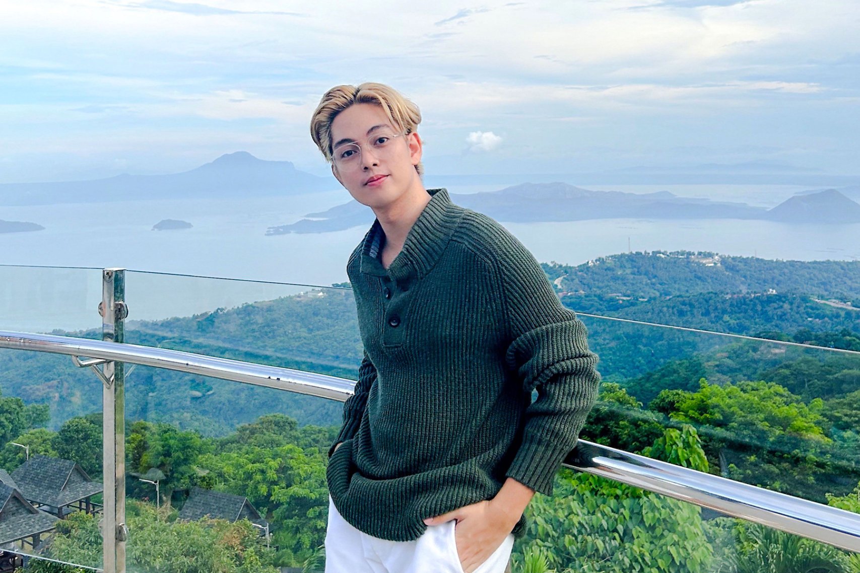 A man with light blond hair wearing green sweater standing at a glass railing
