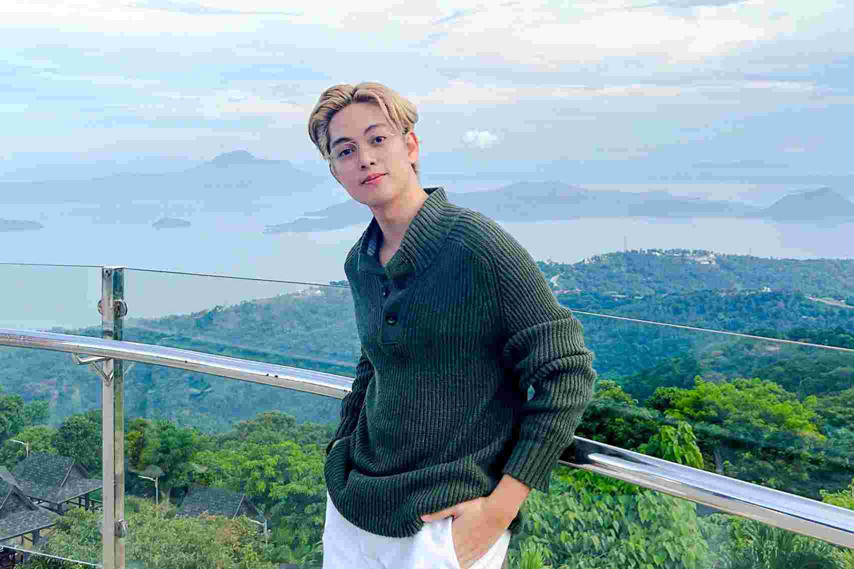 A man with light blond hair wearing green sweater standing at a glass railing
