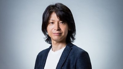 A long hair man wearing black suit on top of a white shirt looking directly ate the camera