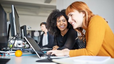 Two smiling women sitting and working on laptop