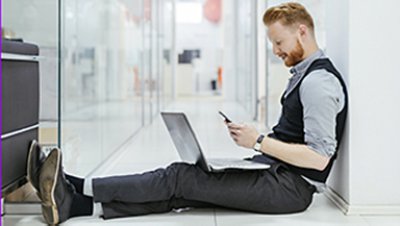 Men sat down on the floor holding his phone and the laptop on top of his knees