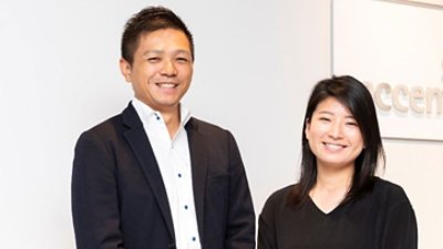 Two people smiling wearing black clothes with Accenture banner in the background