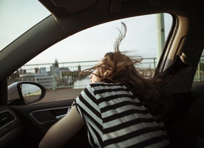 Woman in black and white tshirt in car taking her head outside the window and enjoying