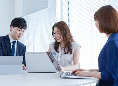 Two women and one man looking at their laptops and smiling