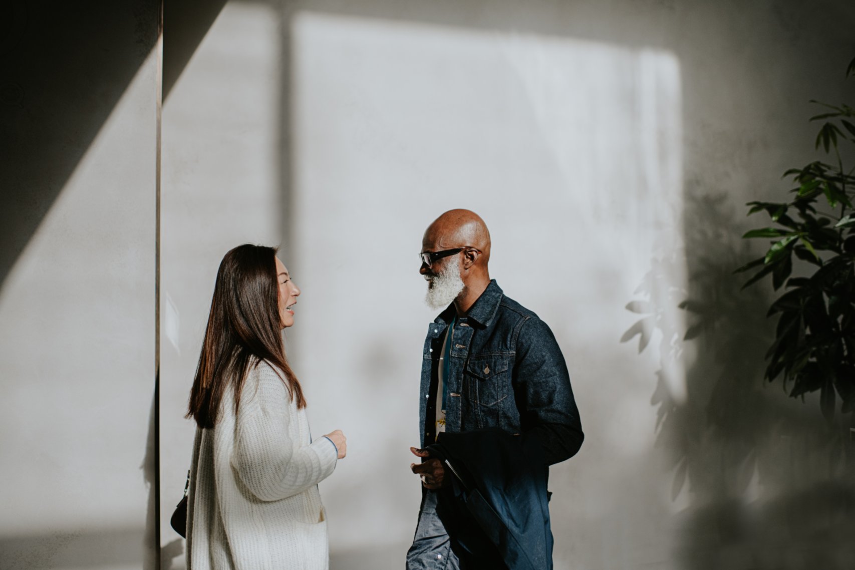 A man and woman stand in a modern interior filled with direct sunlight. They both look at each other. Conceptual with space for copy.