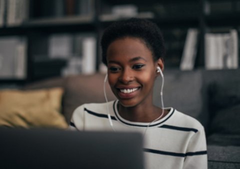 Smiling woman wearing earphones and looking at laptop screen