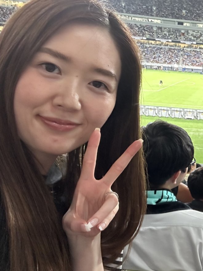 サッカースタジアムを背景にピースサインをするMarikoさん