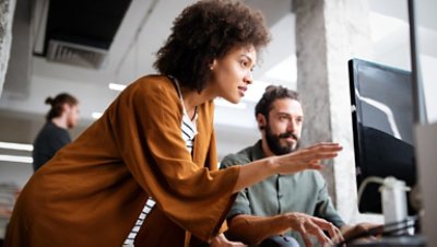 A bearded man and girl with curly hair seems to have a discussion looking on a computer