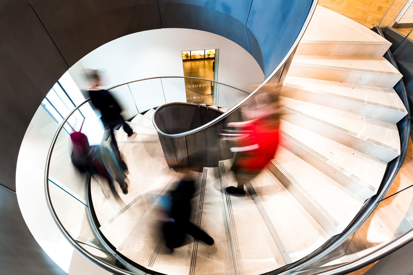 High angle image depicting an abstract view of a group of people running down a modern spiral staircase in the city.
