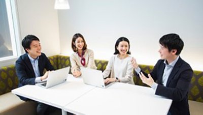 Four people sitting on a brown couch with a white table inside the meeting room while two people operating a laptop