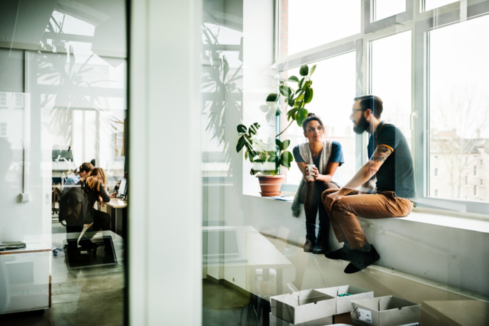 Two young start up business people sitting in a huge office window and talking.