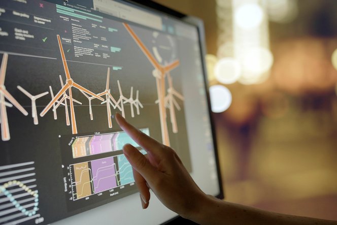 una mano che punta verso le turbine a vento sullo schermo