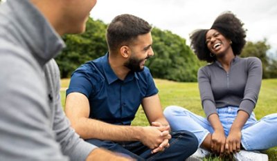 Three people talking and laughing setting on the grass