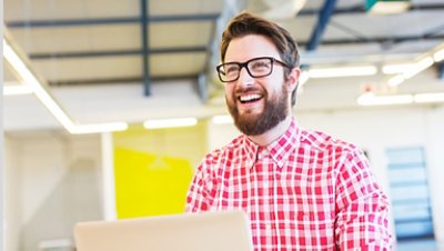 Bearded man smiling with glasses and wearing a red checkered polo