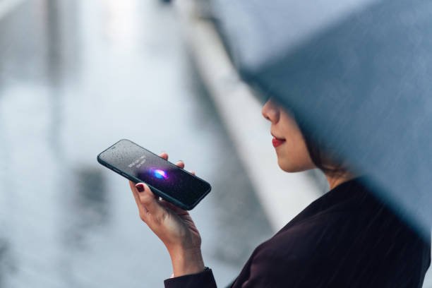 Primo piano di una giovane donna d'affari asiatica che parla con un assistente virtuale su smartphone sotto la pioggia.