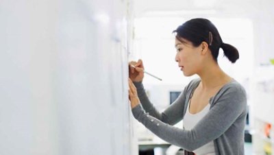 Women on a gray blazer writing on a white board