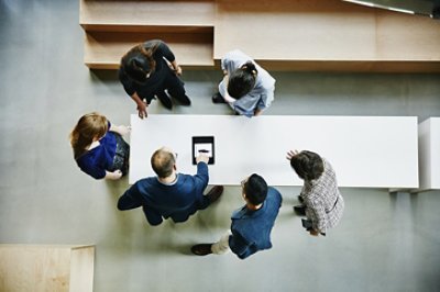 Top view of an office desk where a laptop is there and six people are discussing