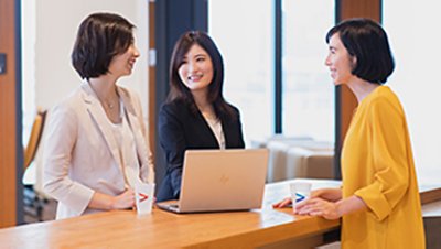 Three girls chating with a laptop on top of the wooden table