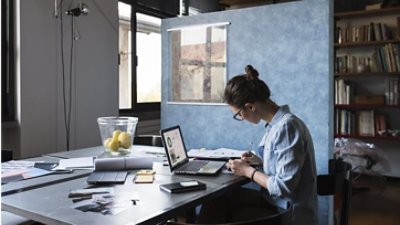 A woman working on his laptop at a computer desk in an office setting