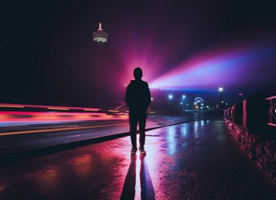 A person standing on the road is illuminated by the light casting a shadow on the ground