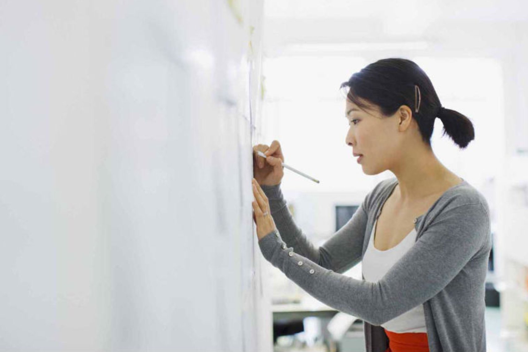 A woman with a short ponytail hair writing on a piece of paper pasted on the wall
