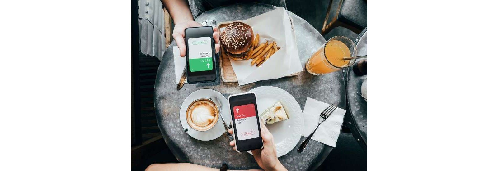 Photograph of a table with food showing a bill being split digitally on their smartphones.