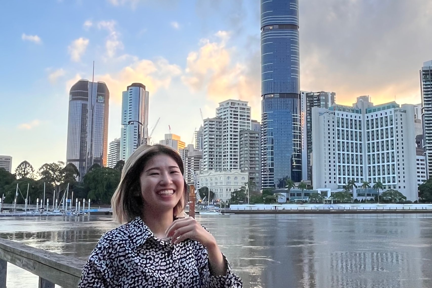 A woman smiling in front of a lake and city buildings