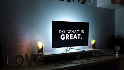 A desktop computer in a dim room with "Do what is great" text flashing on the screen