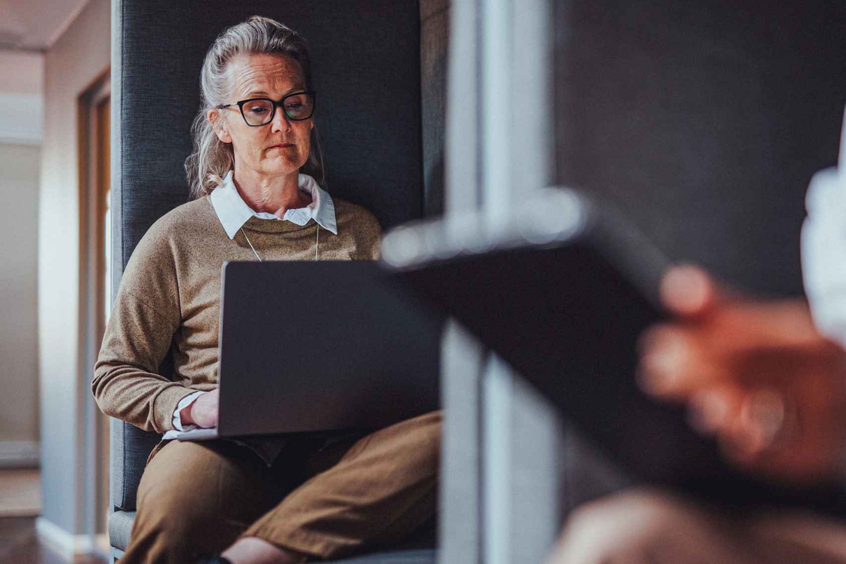 he shot features a mature businesswoman wearing glasses, focused on a laptop screen while working 