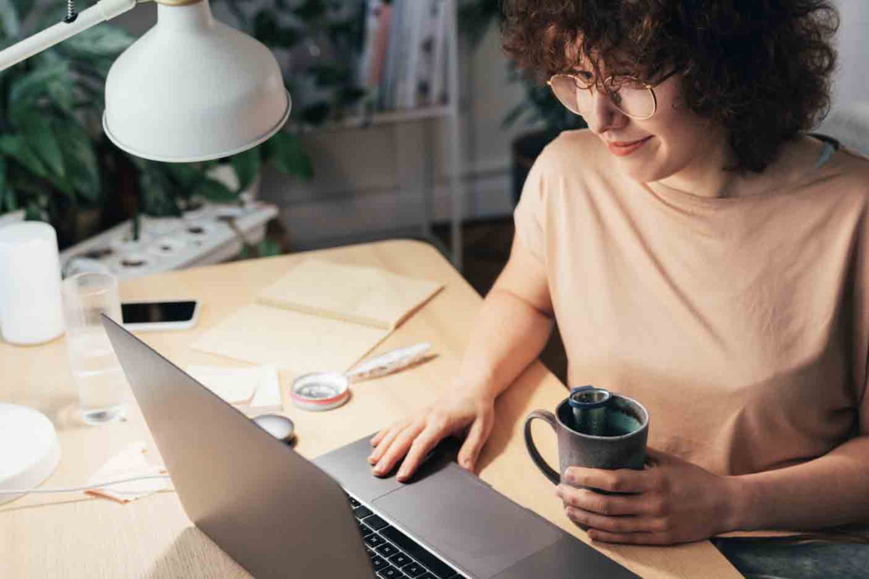 A woman wearing glasses while holding a cup and using her laptop