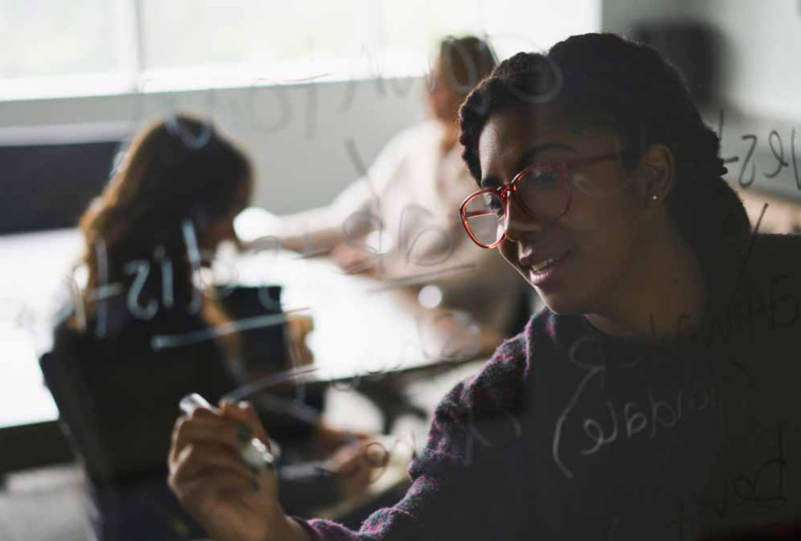 A woman writing on a mirrored board with her teammate at the background