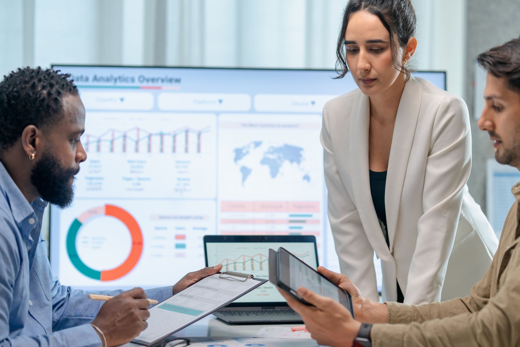 Three marketing professionals work in a conference room looking at marketing analytics on their tablets and computers.
