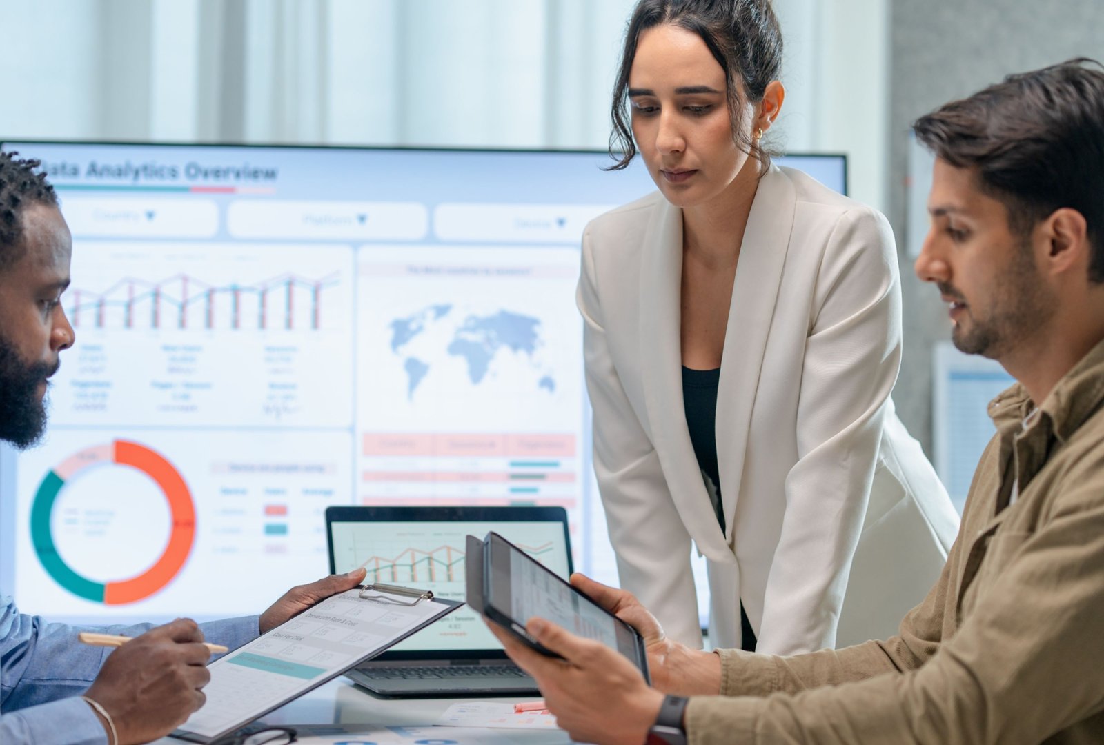 Three marketing professionals work in a conference room looking at marketing analytics on their tablets and computers.