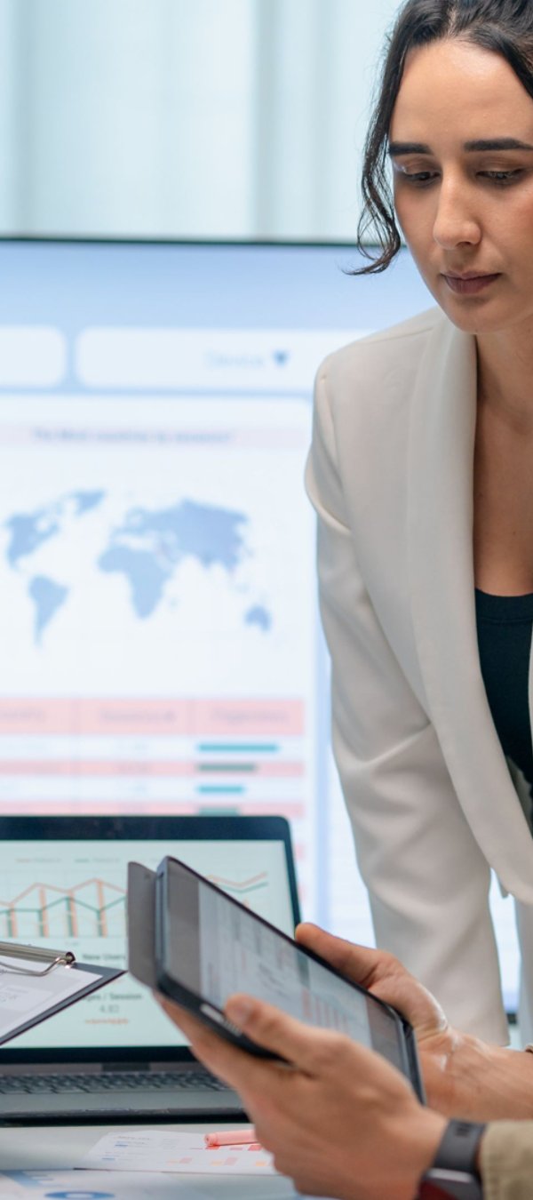 Three marketing professionals work in a conference room looking at marketing analytics on their tablets and computers.