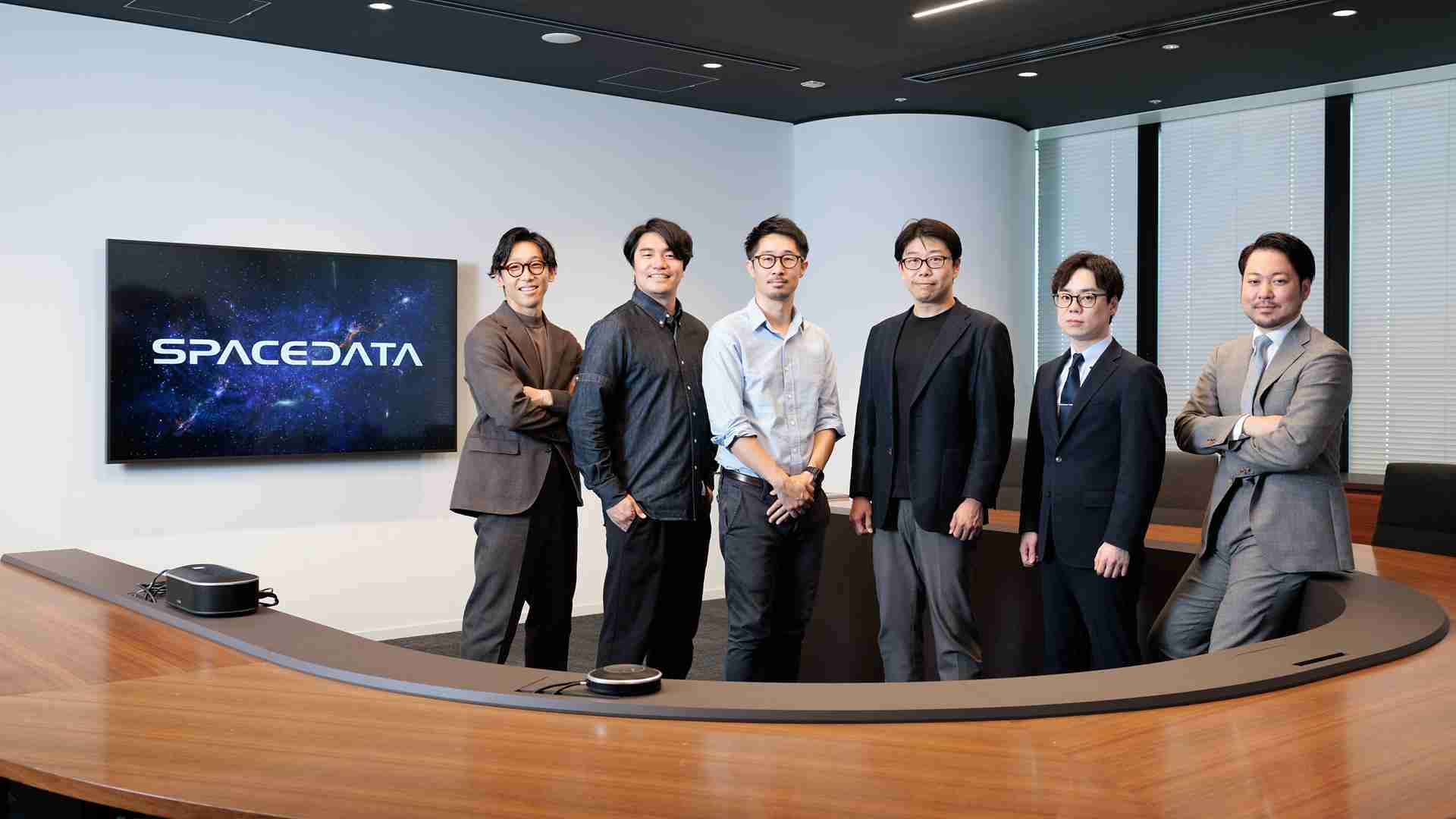 株式会社スペースデータとアクセンチュアのメンバー6名が、SPACEDATAのロゴが映るモニターの前に並んで立っている。