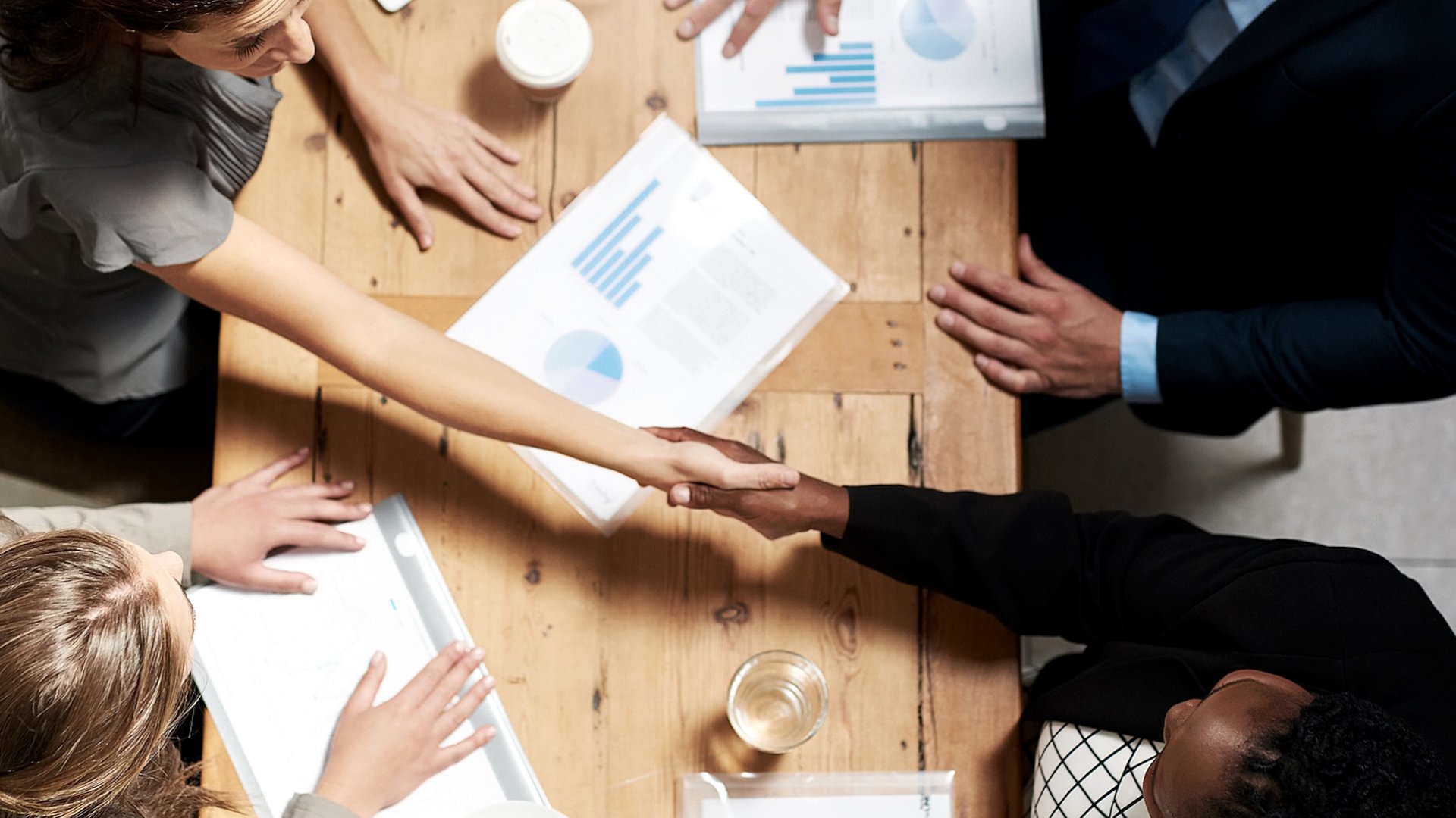 Handshake at a meeting table with charts and coffee.