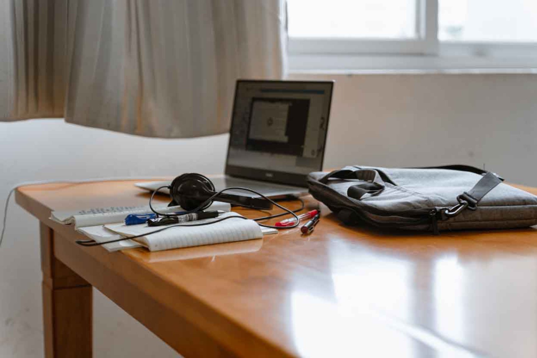 A laptop, bag, headset and other office supplies on top of a wooden table