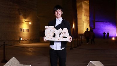 A young architect standing and smiling holding a plaque 