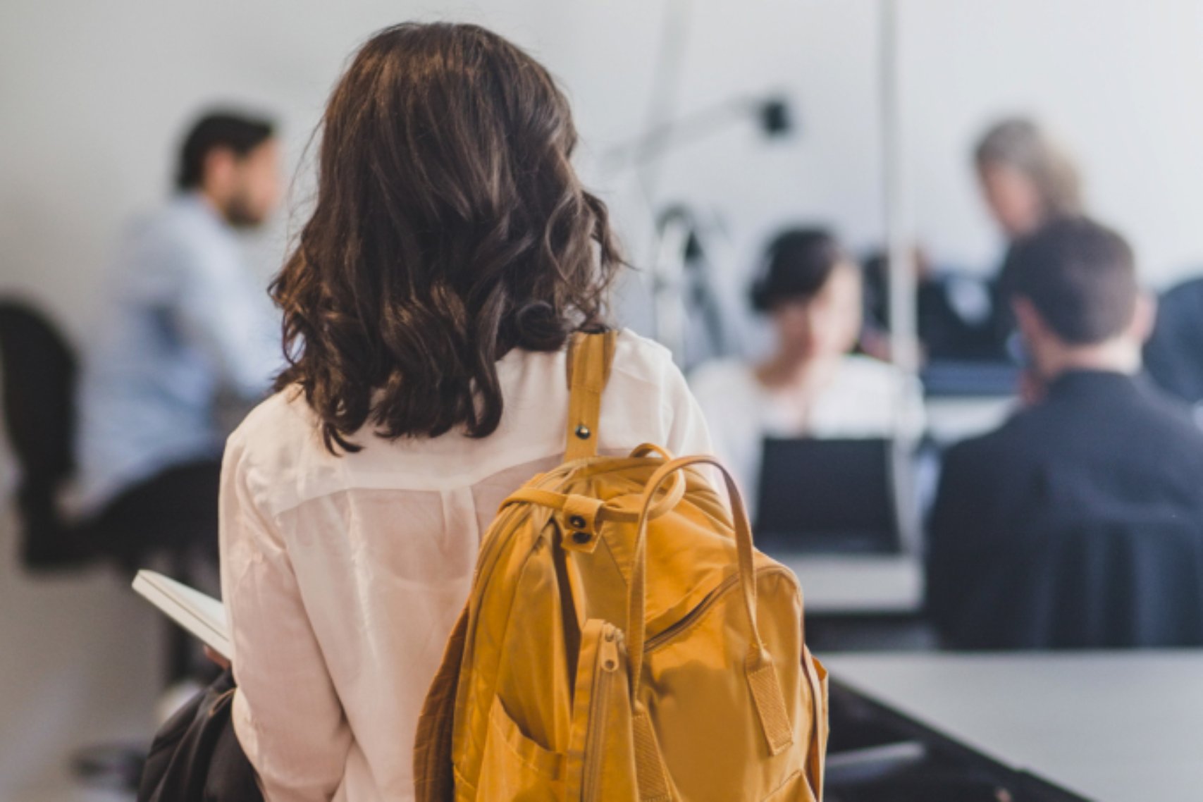 The back view of a girl wearing a yellow backpack going to her class
